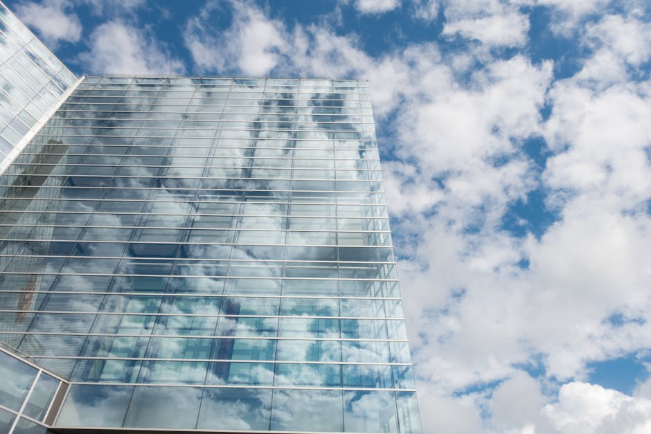 A contemporary skyscraper with glass panels reflecting a bright cloudy sky.